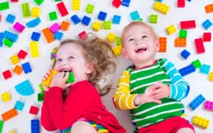Echolalic Speech two kids laying on the bed filled with colorful puzzle pieces and smiling - Autism
