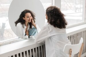 A woman practicing Face Yoga Therapy, looking at herself in the mirror.- Autism Connect