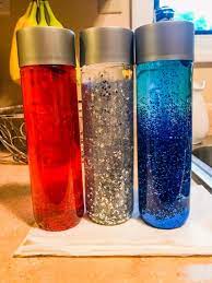 Three glitter-filled water bottles in red, silver, and blue colors, standing on a kitchen countertop.