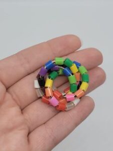 A hand holding a colorful beaded bracelet made from small, multicolored tube beads.