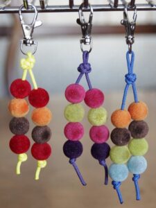 Colorful felt ball keychains hanging from metal clips against a blurred background.