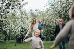 7). A family of four walking through an orchard, surrounded by trees and sunlight. - Autism Connect