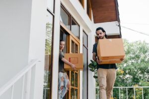 A man and woman carrying boxes into a house. Image relates to 'Relocating with Autism: 10 Steps to Help Autistic Individuals after relocation' -Autism Connect