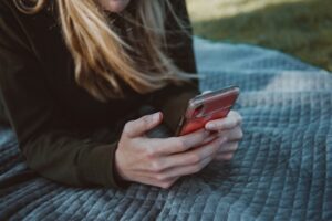  A woman laying on a blanket, using her cell phone- Autism Connect 