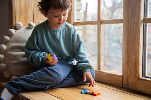 Child playing with building blocks on a windowsill, promoting spinal health through comfortable sitting posture.