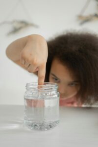 Child touching clear slime in a glass jar, engaging in a sensory activity designed to support autism development.